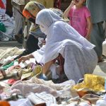 Female customers selecting and purchasing second hand clothes from roadside vendor at Hashtnagri area.