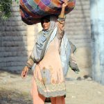 A woman on the way carrying a heavy bundle of dung cake on her head