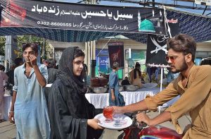 A girl offering water to motorcyclist from sabeel during Chehlum procession to commemorate the martyrdom of Hazrat Imam Hussain (RA) grandson of Holy Prophet Muhammad (SAWW).