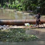 A worker of Irrigation Department cleaning heap of garbage from Rakh Branch Canal.