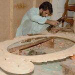 A carpenter is carving different designs on wooden sheet at his workplace