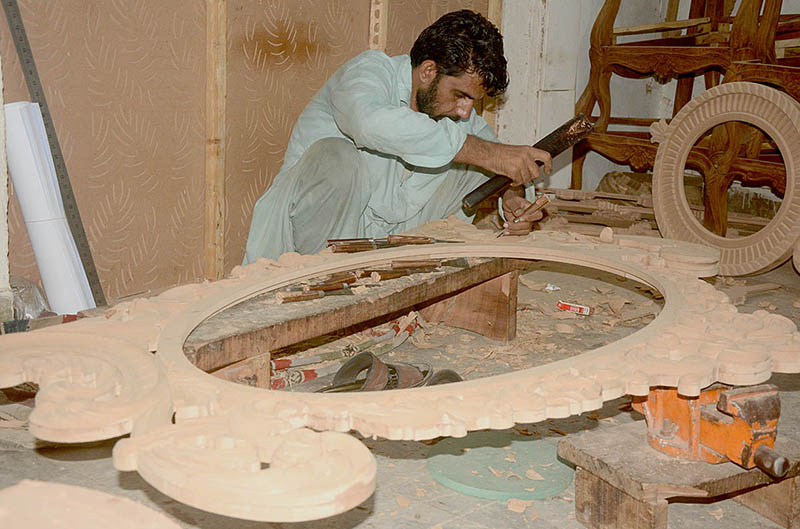 A carpenter is carving different designs on wooden sheet at his workplace