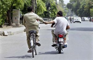 A person sitting on rear seat of motorcycle holding the hand of a cyclist helping him to reach his destination.