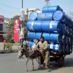 A donkey cart holder loaded with empty drums going towards his destination.