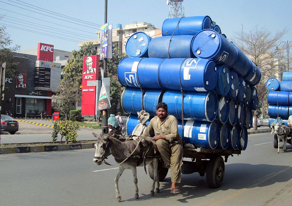 A donkey cart holder loaded with empty drums going towards his destination.