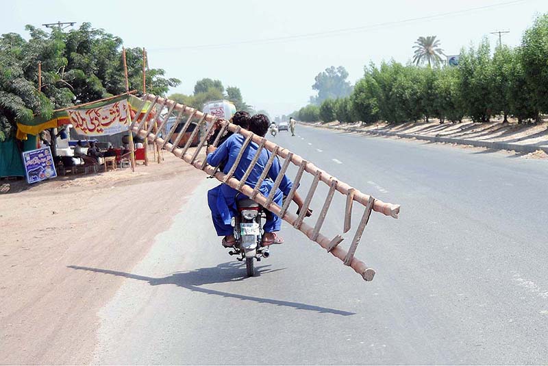 A person holding long ladder while sitting on the rear seat of a motorcycle on the way.