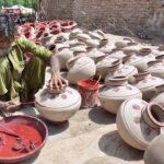 A worker is painting on the clay made pots at his workplace
