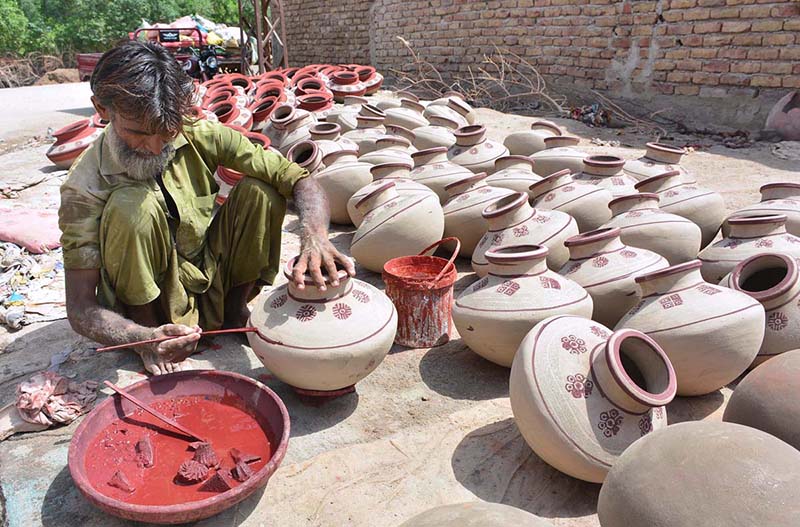 A worker is painting on the clay made pots at his workplace