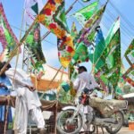 A vendor arranging and displaying Eid Milad-un-Nabi (PBUH) related flags to attract the customer at jail road