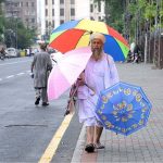 An elderly vendor is selling umbrellas on the footpath