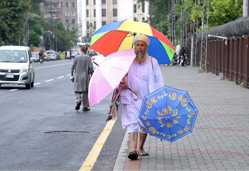 An elderly vendor is selling umbrellas on the footpath
