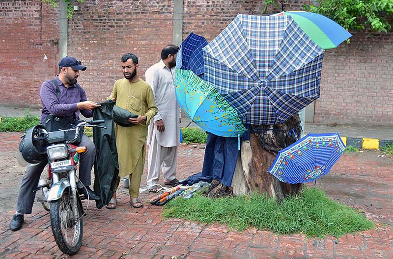 A vendor displays colorful umbrellas and rain suits to customers at his roadside setup during the rainy season