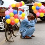 An elderly vendor waiting for customers to sell balloon while sitting near Bus Stop