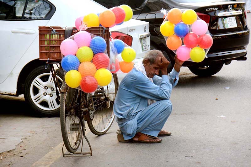 An elderly vendor waiting for customers to sell balloon while sitting near Bus Stop
