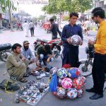 A vendor is selling wallets, watches, and footballs at a roadside stall