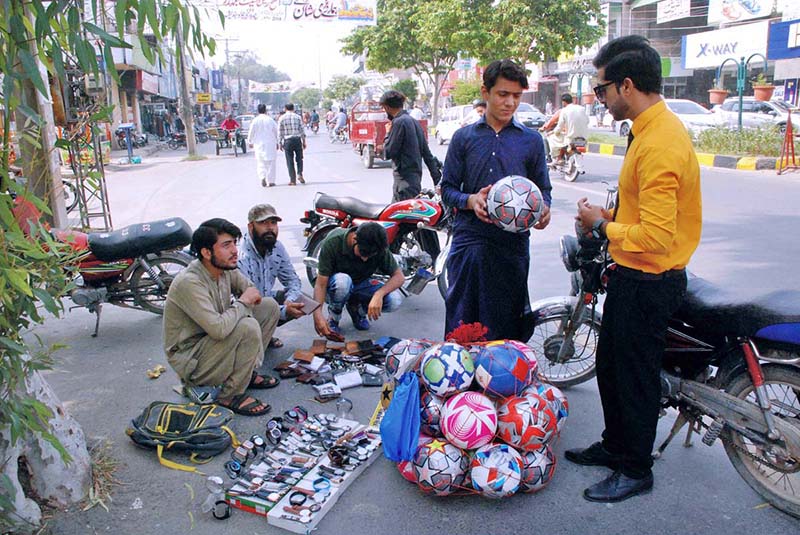 A vendor is selling wallets, watches, and footballs at a roadside stall