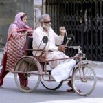 An elderly woman pushing the wheelchair of a disabled person on LMQ Road