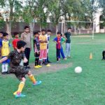 A penalty corner is being taken during a football game at Dring Stadium, with several children aged 10 to 12 participating in the match.