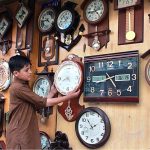 A shopkeeper displaying wall clock in his shop