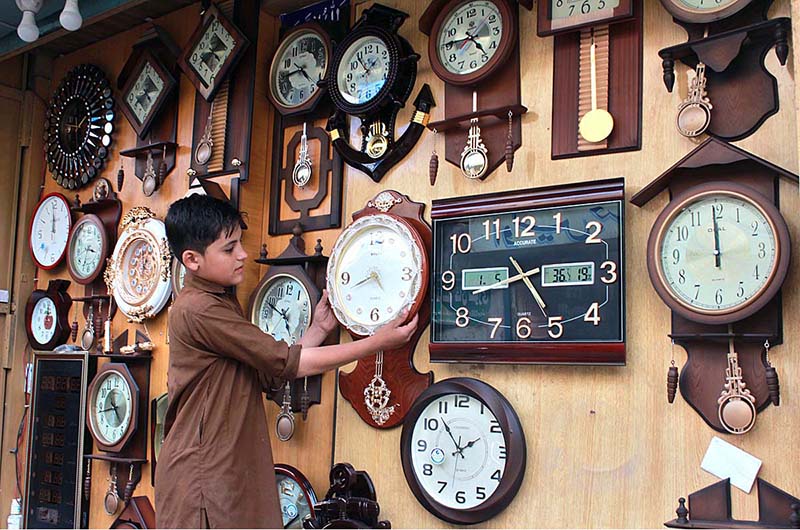 A shopkeeper displaying wall clock in his shop