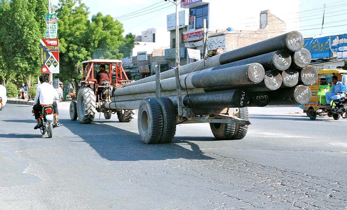 A view of tractor-trolley loaded with electric poles on a road