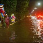An elderly person waiting for customers to sell light baloons while sitting in front of bus stop sheltter during rain in the city