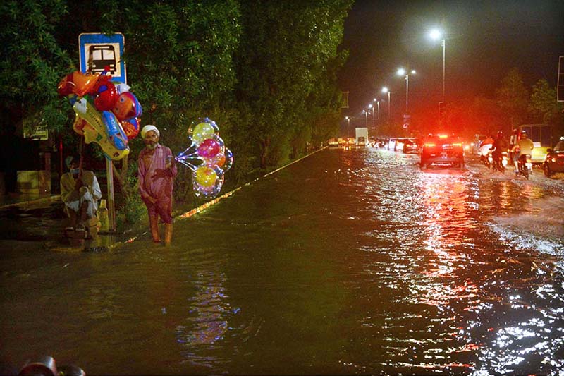 An elderly person waiting for customers to sell light baloons while sitting in front of bus stop sheltter during rain in the city