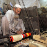 Worker busy in coloring on the part of a traditional bed (charpai) at his workplace