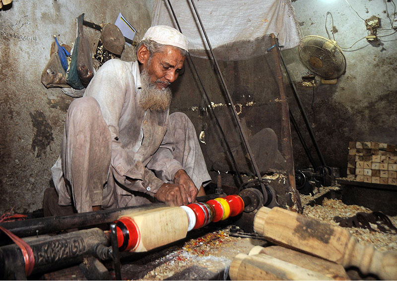 Worker busy in coloring on the part of a traditional bed (charpai) at his workplace