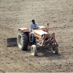 Farmer busy in leveling his farm field with the help of tractor for next crop