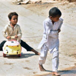 Children enjoying while play with toy vehicle on the road at Latifabad.
