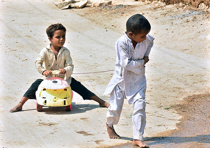 Children enjoying while play with toy vehicle on the road at Latifabad.