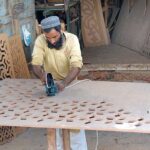 Worker busy in carving designs on the wooden sheet with the help of a machine at his workplace.