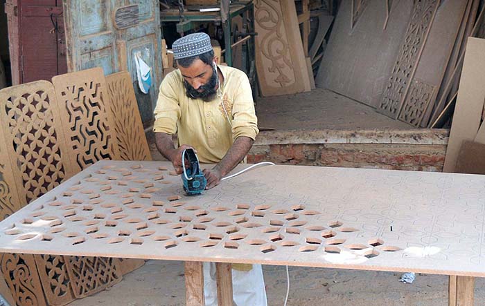 Worker busy in carving designs on the wooden sheet with the help of a machine at his workplace.