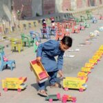 A young boy displaying handmade wooden toys and plastic chairs to attract the customers at his roadside setup