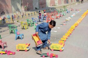 A young boy displaying handmade wooden toys and plastic chairs to attract the customers at his roadside setup