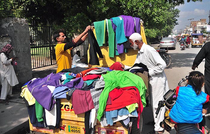 People selecting and purchasing warm clothes from roadside stall in front of Municipal Corporation.