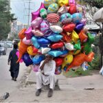 An elderly vendor waiting for customers to sell different shapes balloons while sitting at roadside in Federal Capital