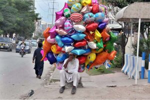 An elderly vendor waiting for customers to sell different shapes balloons while sitting at roadside in Federal Capital