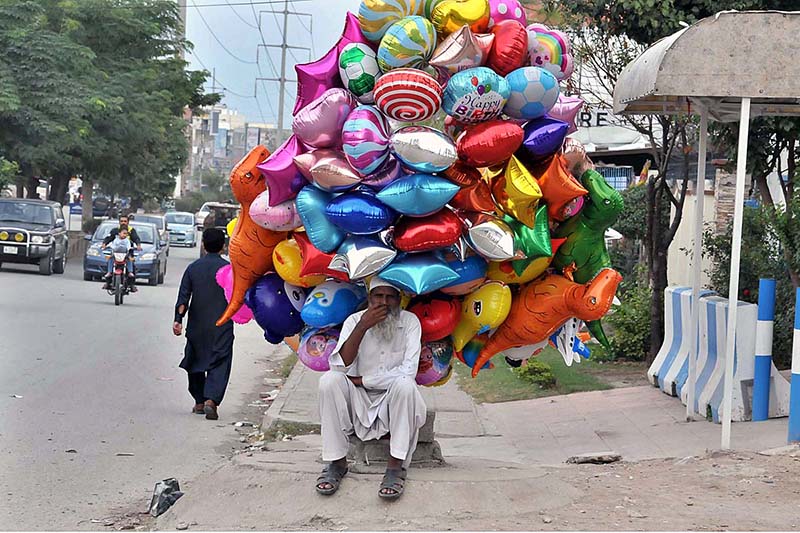 An elderly vendor waiting for customers to sell different shapes balloons while sitting at roadside in Federal Capital