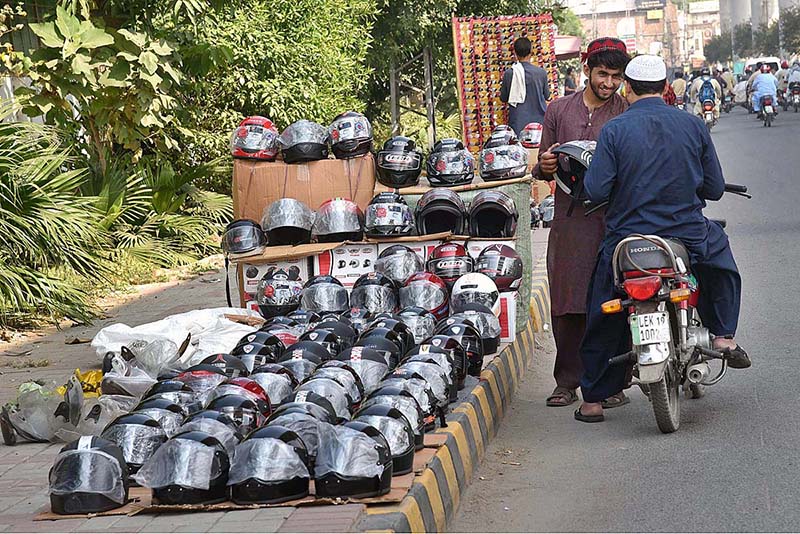 A motorcyclist purchasing a helmet from a roadside vendor in the city
