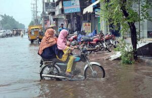 Girl bike rider with family passing through the stagnant water at Sargodha Road after heavy rain in the city.