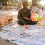 A vendor waiting for customers to sell balloon while sitting near mall road