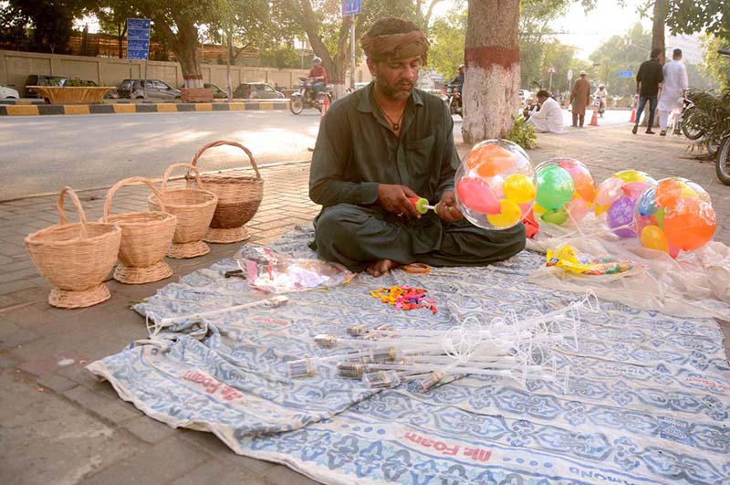 A vendor waiting for customers to sell balloon while sitting near mall road