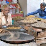 Vendor busy in roasting grams for the customers at his roadside setup.