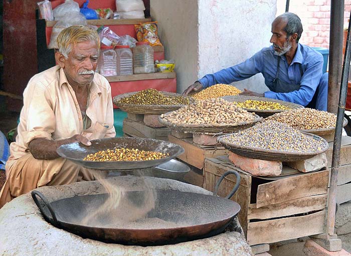 Vendor busy in roasting grams for the customers at his roadside setup.