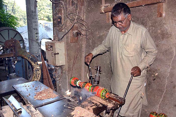 A carpenter busy in making part of a traditional bed (charpai) at his workplace.