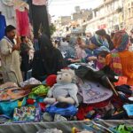 Women selecting and purchasing secondhand clothes displayed by roadside vendors