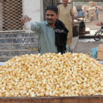 A vendor is busy sprinkling water on the pieces of sugarcane to keep them fresh at his handcart