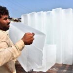 A laborer busy in unloading ice block from a delivery rickshaw at his roadside setup in the city.